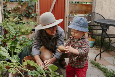 Toddler boy with potato standing by mother in in back yard