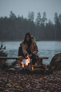 Portrait of young woman sitting by campire at lakeshore