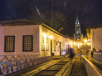 Illuminated railroad tracks by buildings in city at night