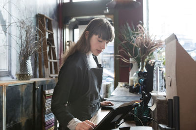 Confident young female owner using digital tablet at counter in store