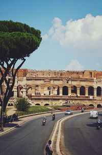 Road passing through city against cloudy sky