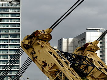 Low angle view of crane by building against sky