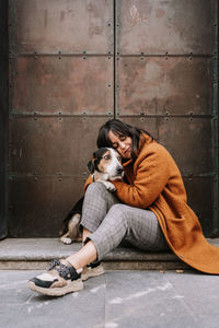 Side view of female owner gently embracing treeing walker coonhound dog while sitting on street in city