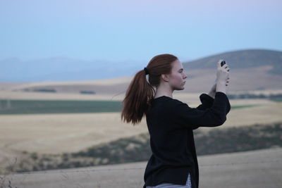 Side view of woman photographing while standing on field