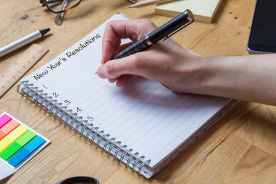 Cropped hand holding pen over spiral notebook with new year resolution text on table