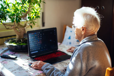 Rear view of senior woman using laptop while sitting at home