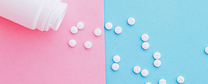 Directly above shot of pills spilling from bottle against blue background