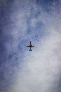 Low angle view of airplane flying against cloudy sky