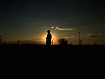 Silhouette man standing on field against sky at sunset