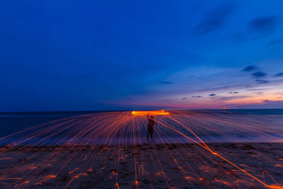 Silhouette of man with illuminated wire wool standing at beach during sunset