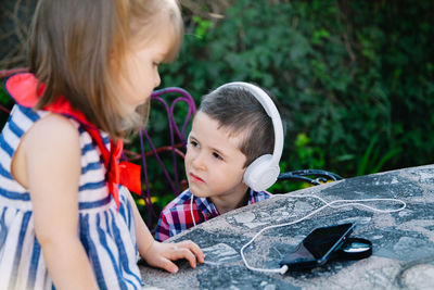 Cute boy listening music with sister at table