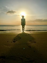 Rear view of man standing on beach against sky during sunset