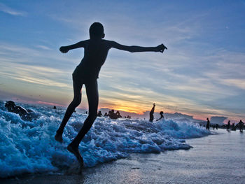 Silhouette man with arms raised on beach against sky during sunset