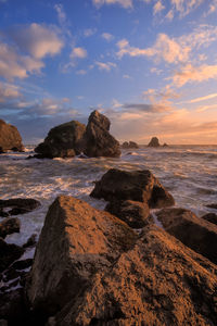 Rocks on beach against sky during sunset