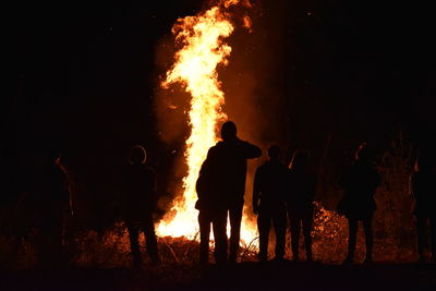 People standing by fire on field at night