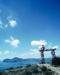 Man sitting on built structure by sea against blue sky