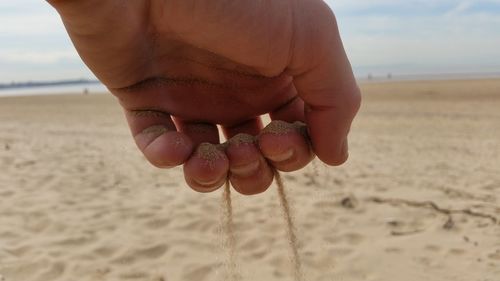 Close-up of hand holding sand at beach against sky