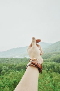 Cropped hand over mountain against clear sky