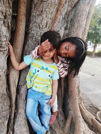 Siblings standing by tree trunk