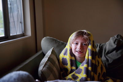 Portrait of smiling boy with blanket on sofa at home