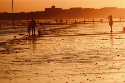 Silhouette people walking on beach against sky during sunset