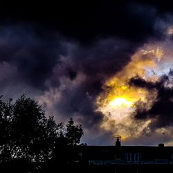 Low angle view of silhouette trees and building against dramatic sky