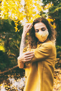 Mature woman wearing mask standing against autumn leaves