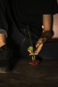 Low section of person holding rose while sitting on floor
