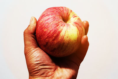 Close-up of hand holding apple against white background