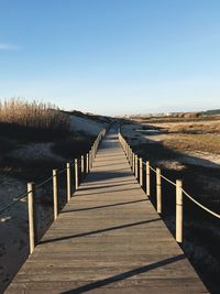 Wooden footbridge leading towards beach against clear sky