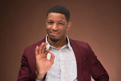 Portrait of smiling man gesturing ok sign against brown background