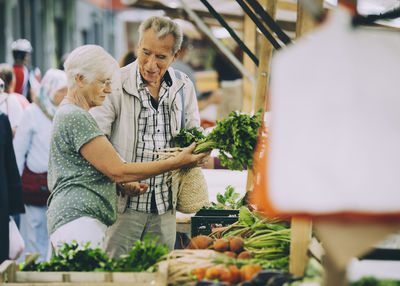 Senior woman shopping for vegetables with partner at street market in city