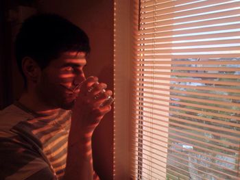 Close-up of young man looking through window at home