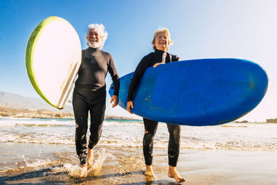 Man and woman walking with surfboards on beach against clear sky