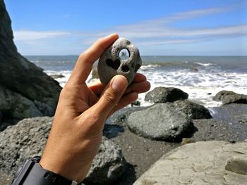 Close-up of hand holding rock at beach against sky