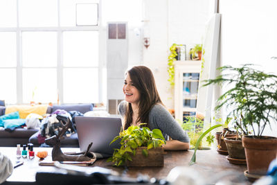 Smiling young woman using laptop while looking away at table in living room