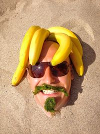 Directly above shot of cheerful man with seaweed and bananas buried in sand