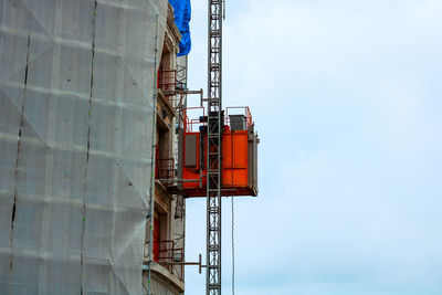 Low angle view of crane at construction site against sky