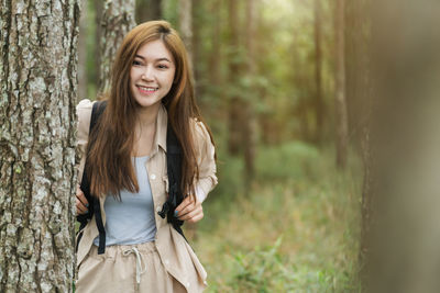 Portrait of young woman standing against tree