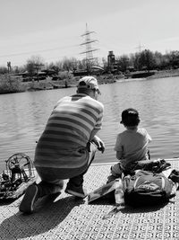 Rear view of men sitting on lake against sky