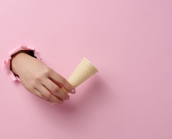 Empty waffle cone ice cream cup in a woman's hand sticking out of a torn hole in a pink paper