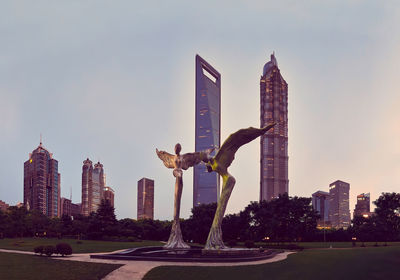 Statue by modern buildings against sky in city