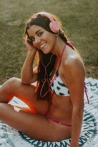 Portrait of smiling young woman in bikini sitting on land