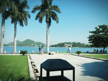 People at park by sea against clear blue sky