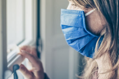 Woman looking outside the window with surgical mask during coronavirus lockdown. covid-19 people