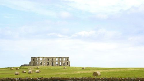 Hay bales on field by castle against sky