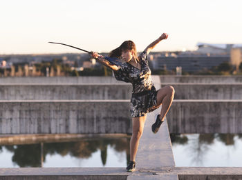 Female athlete practicing sword on structure against clear sky at sunset
