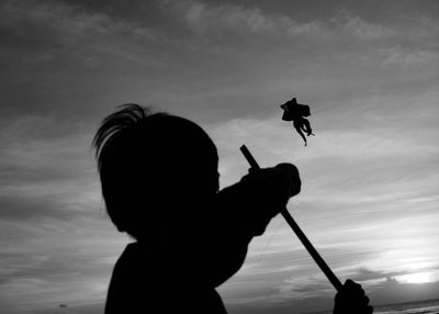 Silhouette people holding kite against sky during sunset