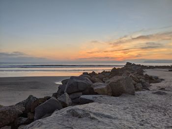 Rocks on beach against sky during sunset