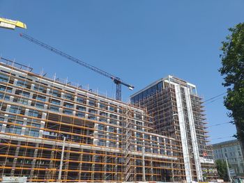 Low angle view of crane by building against clear blue sky